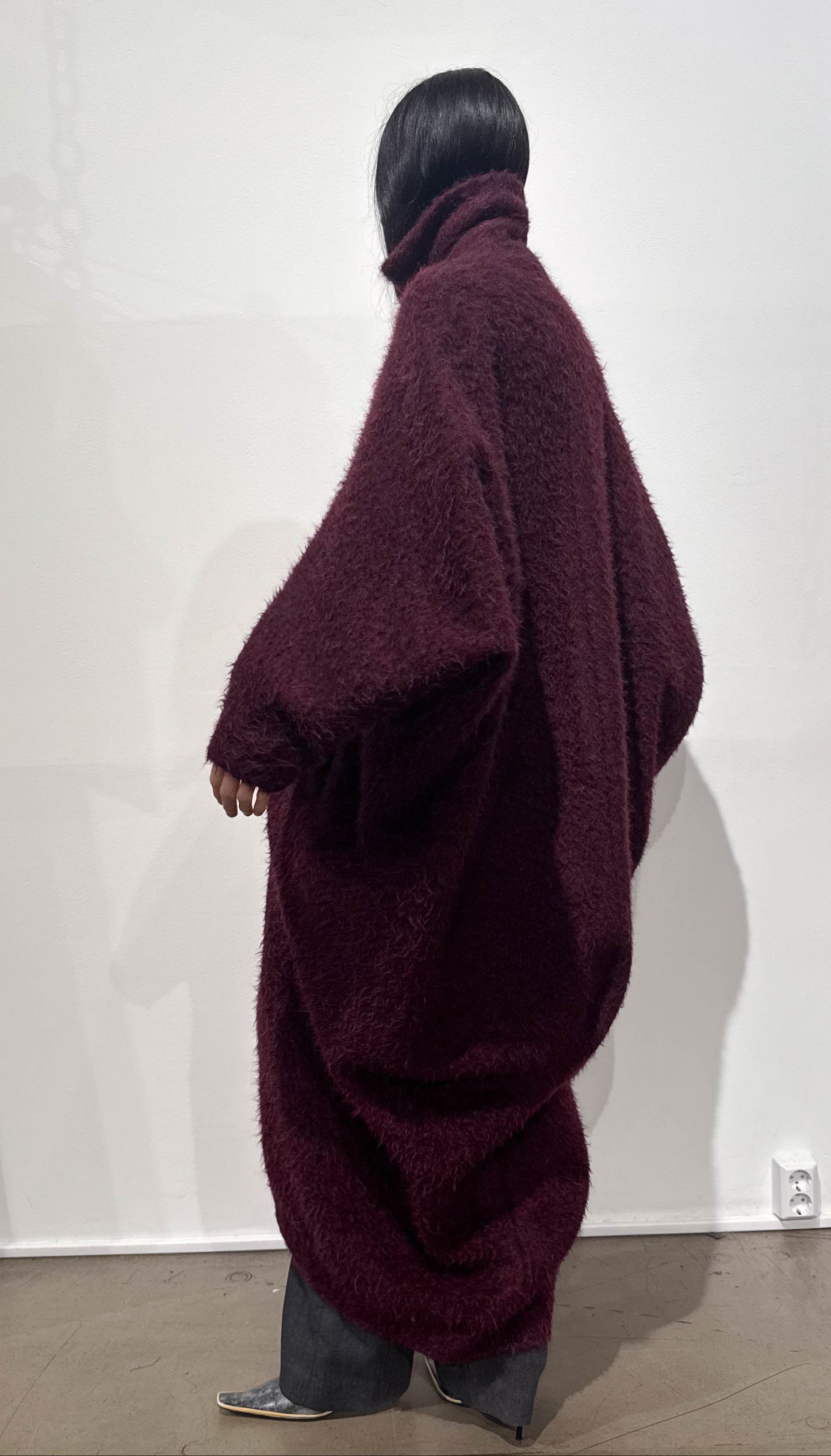 Person wearing a large burgundy sweater against a white wall.