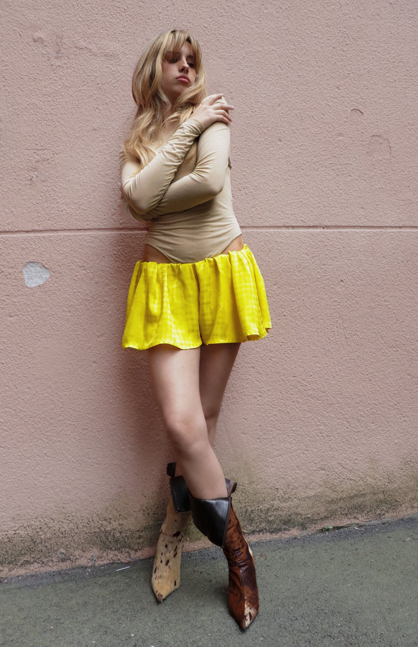 Person wearing a yellow skirt and beige top against a pink wall.