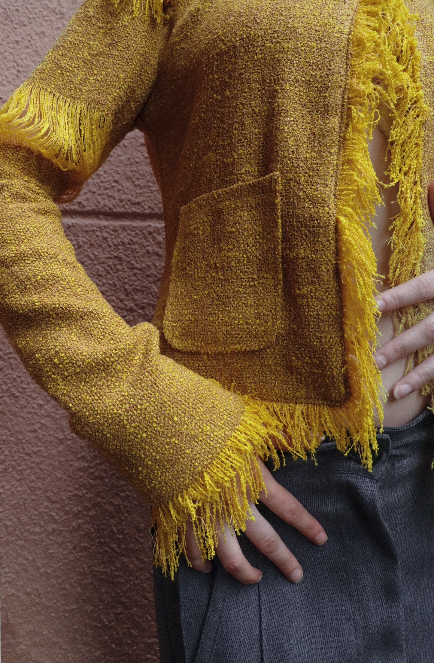 Yellow textured jacket with fringes worn by a person against a pink wall.