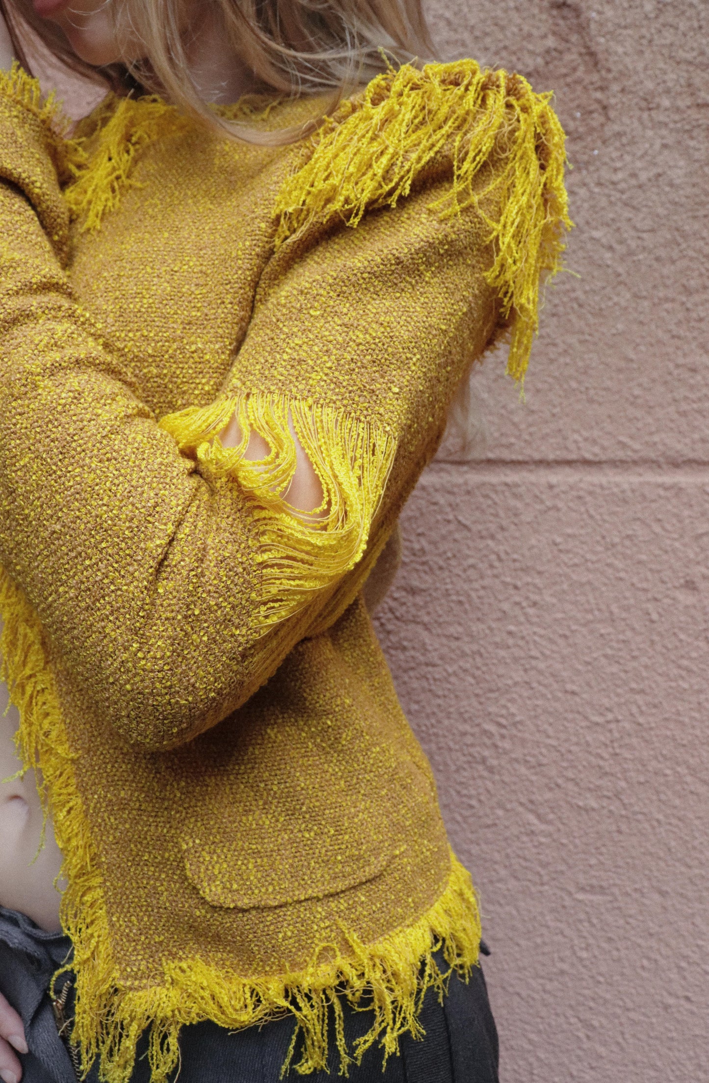 Yellow textured jacket with frayed edges worn by a person against a pink wall.