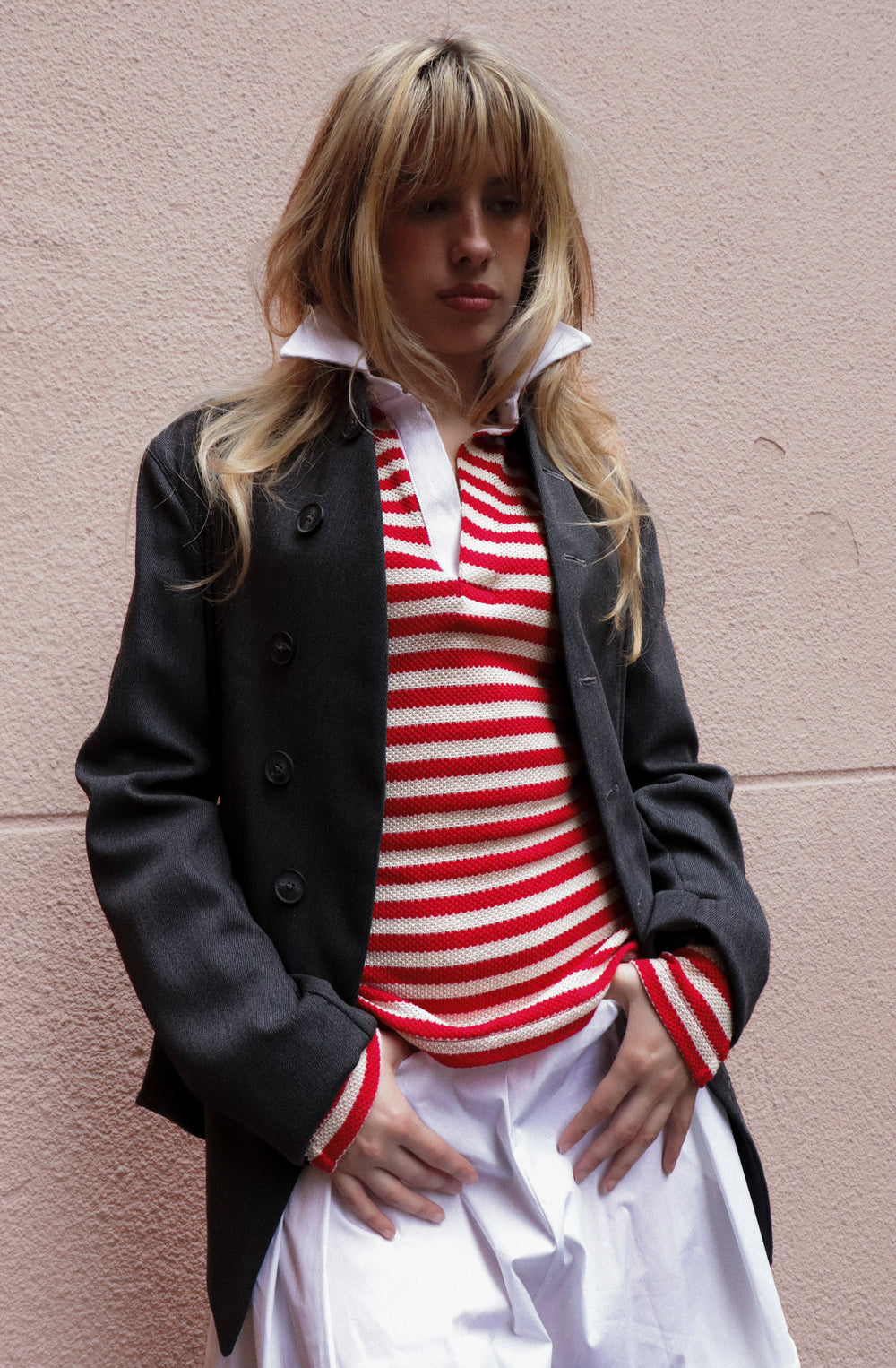 Person wearing a black coat over a red and white striped shirt against a pink wall.