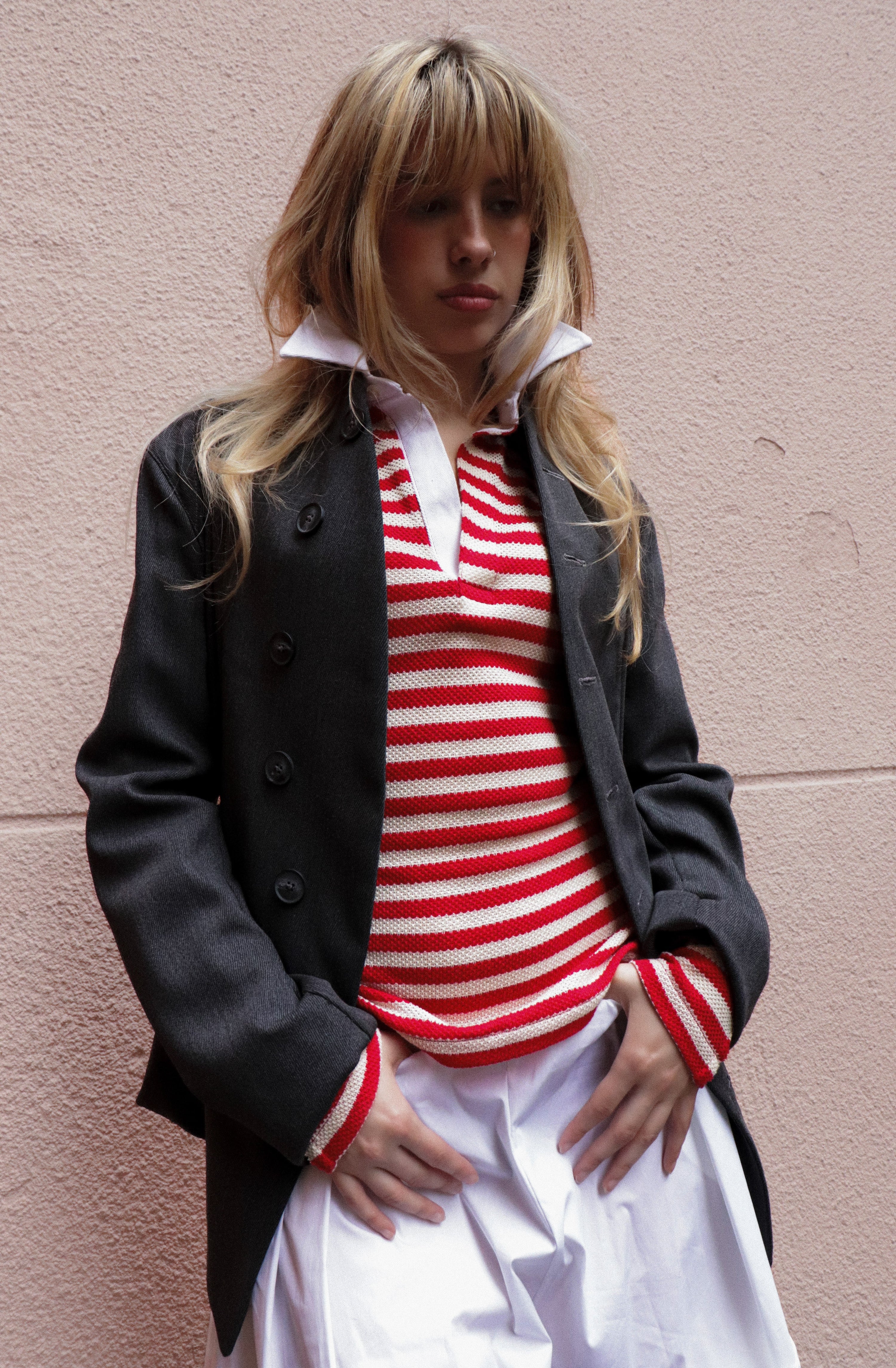 Person wearing a black coat over a red and white striped shirt against a pink wall.