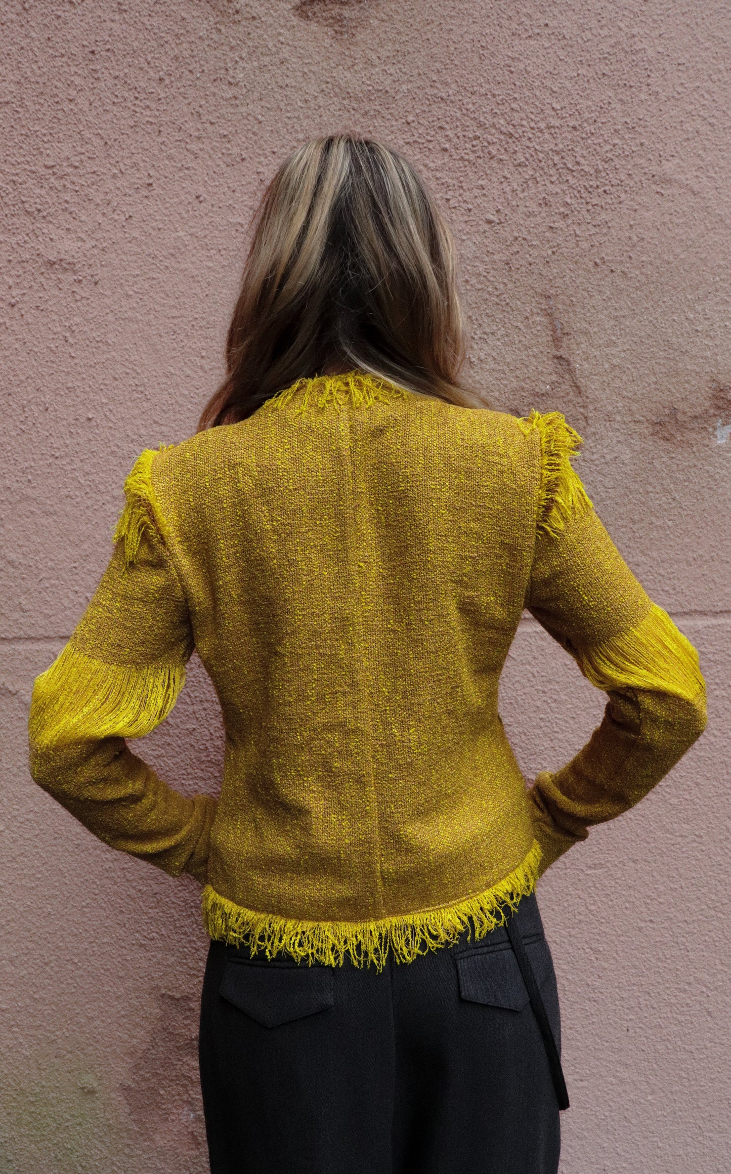 Person wearing a yellow textured jacket against a pink wall